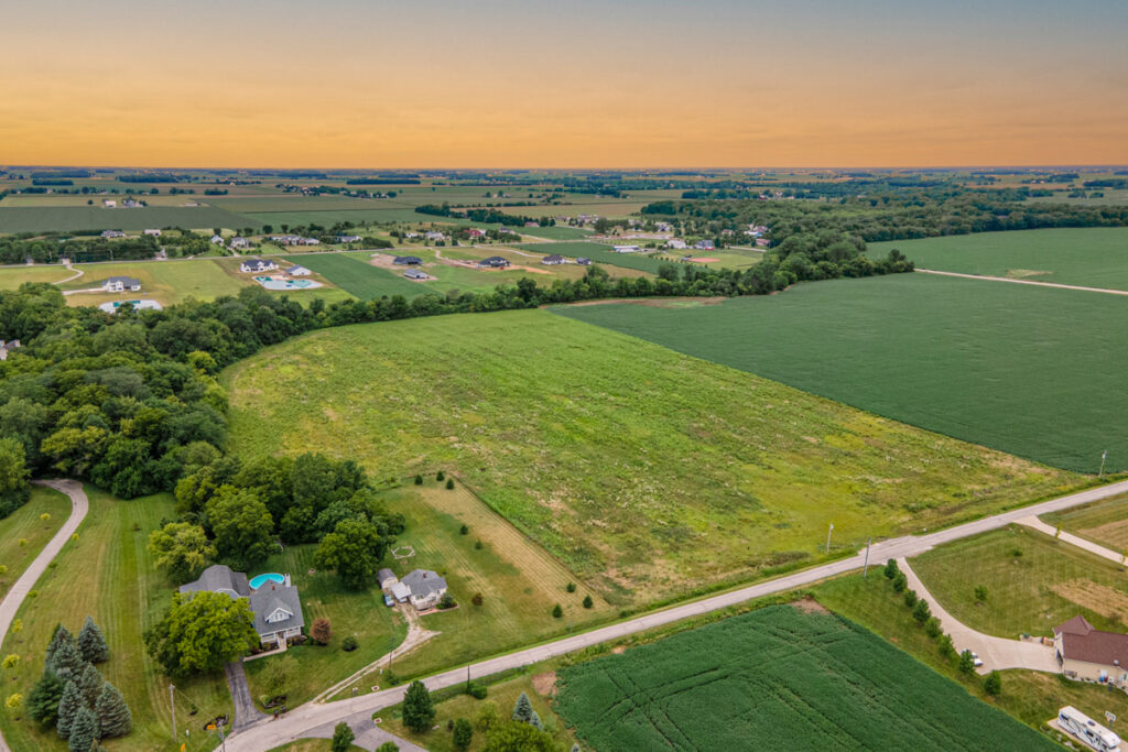 Aerial photograph of homes, roads and green fields beneath a warm sunset.